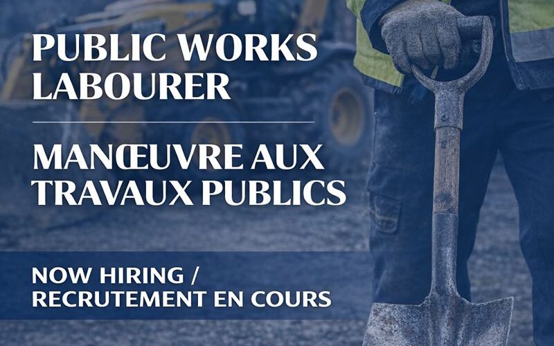 A worker holds a shovel in front of a back hoe. The image advertises a new job opportunity for a public works labourer.